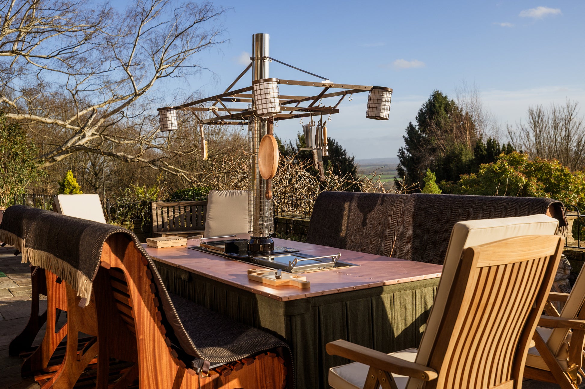 Outdoor dining area with wooden table and chairs, surrounded by trees and a clear sky.