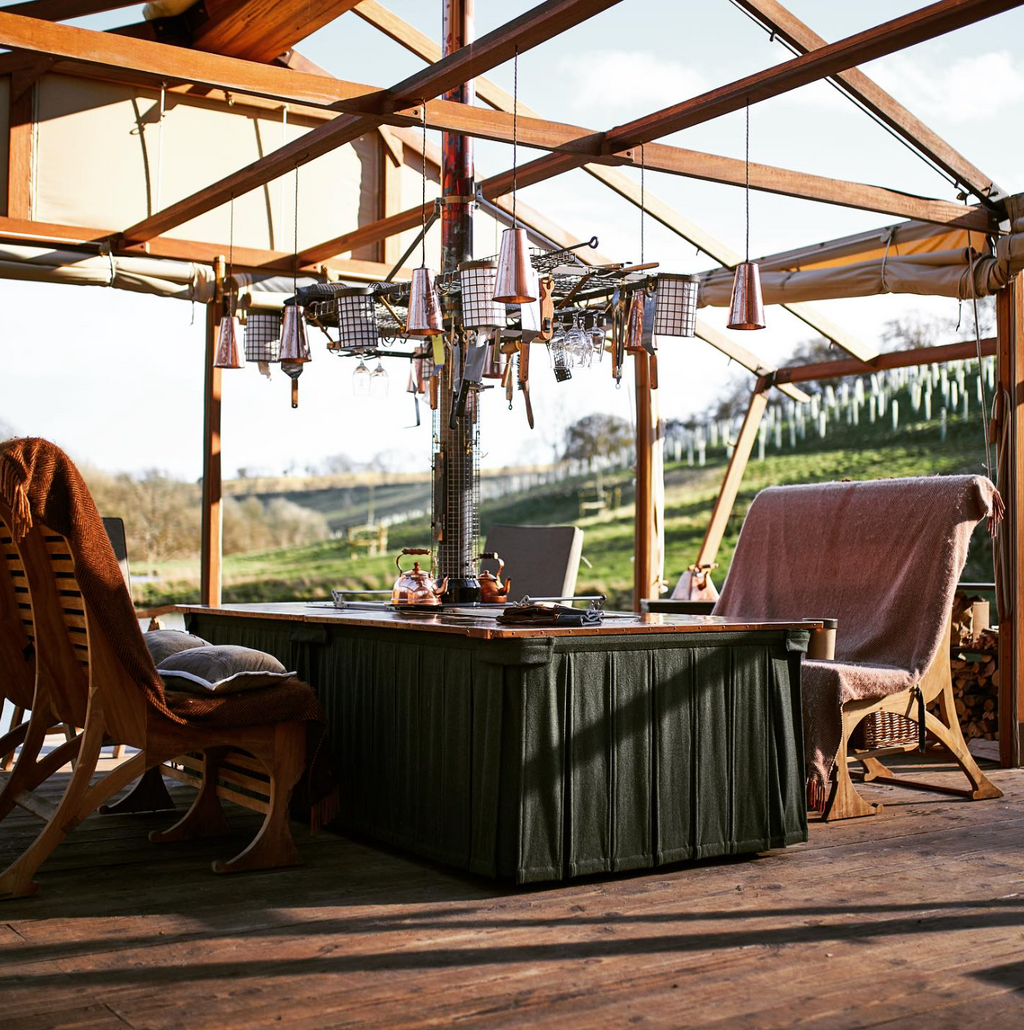 Indoor setting with wooden beams, a table, chairs, and a view of greenery outside.